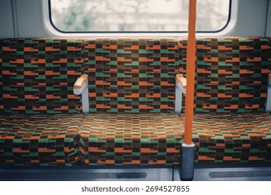 Close-up of empty patterned seats on a London Overground train, showing the distinctive orange and green moquette fabric design.