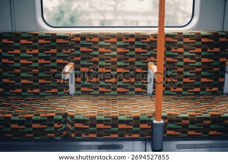 Close-up of empty patterned seats on a London Overground train, showing the distinctive orange and green moquette fabric design.