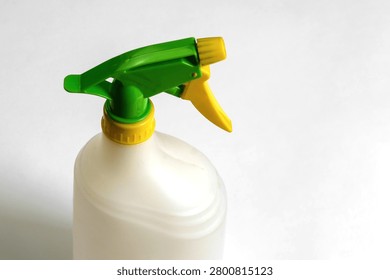 Close-up of an empty white plastic trigger spray bottle with green and yellow adjustable nozzle isolated on white background, reusable household cleaning container.