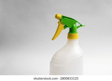 Close-up of an empty white plastic trigger spray bottle with green and yellow adjustable nozzle isolated on white background, reusable household cleaning container.