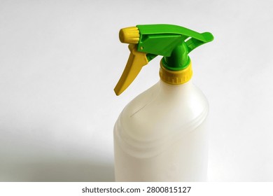 Close-up of an empty white plastic trigger spray bottle with green and yellow adjustable nozzle isolated on white background, reusable household cleaning container.