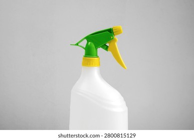 Close-up of an empty white plastic trigger spray bottle with green and yellow adjustable nozzle isolated on white background, reusable household cleaning container.