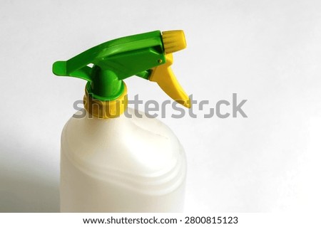 Close-up of an empty white plastic trigger spray bottle with green and yellow adjustable nozzle isolated on white background, reusable household cleaning container.