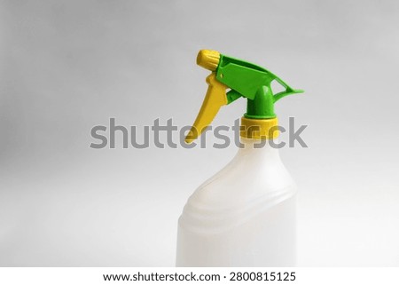 Close-up of an empty white plastic trigger spray bottle with green and yellow adjustable nozzle isolated on white background, reusable household cleaning container.