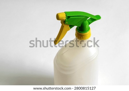 Close-up of an empty white plastic trigger spray bottle with green and yellow adjustable nozzle isolated on white background, reusable household cleaning container.