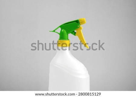Close-up of an empty white plastic trigger spray bottle with green and yellow adjustable nozzle isolated on white background, reusable household cleaning container.