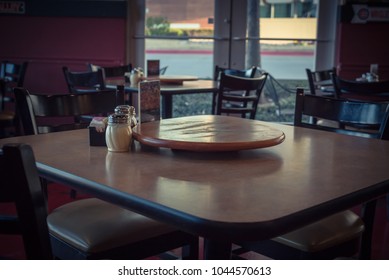 Close-up Empty Wooden Table With Rotating Serving Plate And Shaker Seasonings. Red Pepper Flakes, Parmesan, Black Pepper, Salt. Vintage Tone