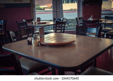 Close-up Empty Wooden Table With Rotating Serving Plate And Shaker Seasonings. Red Pepper Flakes, Parmesan, Black Pepper, Salt. Vintage Tone