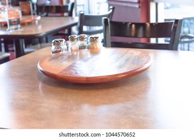 Close-up Empty Wooden Table With Rotating Serving Plate And Shaker Seasonings. Red Pepper Flakes, Parmesan, Black Pepper, Salt. Vintage Tone