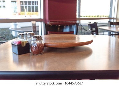 Close-up Empty Wooden Table With Rotating Serving Plate And Shaker Seasonings. Red Pepper Flakes, Parmesan, Black Pepper, Salt.