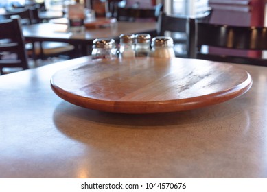 Close-up Empty Wooden Table With Rotating Serving Plate And Shaker Seasonings. Red Pepper Flakes, Parmesan, Black Pepper, Salt.