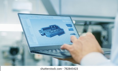 Close-up Of The Engineer Holding Laptop With CAD Component Model On Screen. In The Background Modern Factory Equipment.