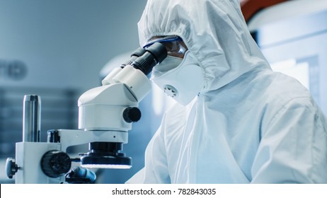 Close-up of the Engineer/ Technician/ Scientist Checking Component under the Microscope. He Wears Sterile Coverall Suit and Protective Glasses While Working a Project.