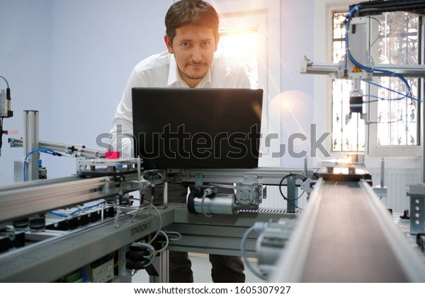 Close-up of Engineer is working on laptop to\
programming PLC of smart factory and automated car on production\
line is waiting. Industry 4.0 concept; artificial intelligence in\
smart factory.