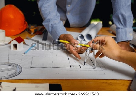 Close-up of engineers collaborating on architectural blueprint with pencil and compass, focusing on precision and teamwork in construction planning.