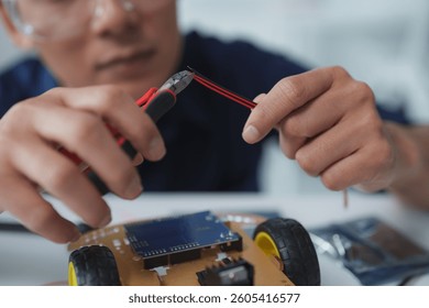 Close-up of engineer's hands using wire cutters on a red and black wire while building a robot prototype in a laboratory setting, showcasing innovation and technological development