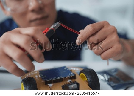 Close-up of engineer's hands using wire cutters on a red and black wire while building a robot prototype in a laboratory setting, showcasing innovation and technological development