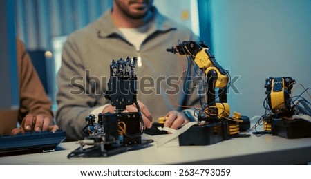 Close-up of engineers working on robotic arms in a modern tech workspace. Focus on hardware development, coding, and robotics prototyping.