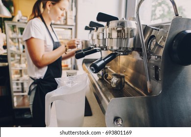 Closeup of espresso machine making coffee. Thin stream flow coming pouring to metal mug jug. Barista woman on the background blurry. Toned with warm yellow film filters. - Powered by Shutterstock