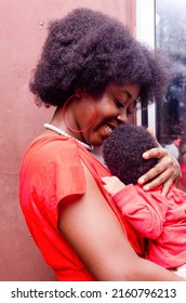 Closeup Of Excited Black Young Woman With A Child Isolated Over Red Background, Wearing Red Dress And Full Dark Hair