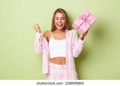 Close-up Of Excited Blond Girl Dancing From Happiness, Receiving Gift In Box And Dancing, Standing Over Green Background Upbeat