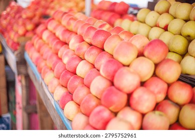 A close-up, eye-level shot captures rows of red, golden, and green apples arranged diagonally on a rustic wooden stall with a faded blue edge. The shallow depth of field emphasizes the glossy texture and natural imperfections of the fruit, while the background dissolves into soft color blocks. The scene evokes quiet abundance and the dignity of local commerce in a Malawian market setting.