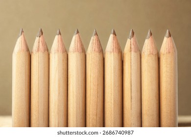A close-up, eye-level view of a line of sharpened, uncolored wooden pencils against a neutral background.