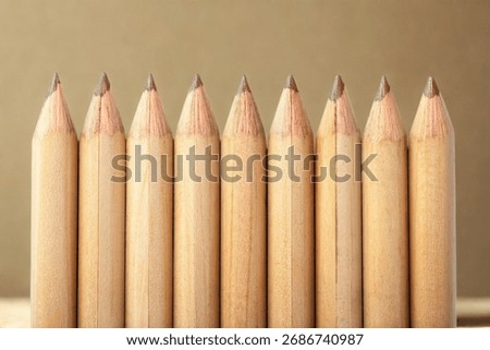 A close-up, eye-level view of a line of sharpened, uncolored wooden pencils against a neutral background.