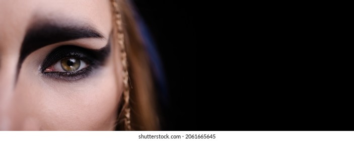 Close-up Of Eyes With Halloween Makeup. Celtic Goddess Harpy Costume Smokey Eye. Carnival Banner. Copy Space Black Background. Magical Witch. Macro Eyes And Make-up.