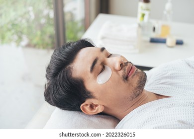 Closeup Face, Asian Man Relaxation In Spa Salon With Eye Mask For Under Eye Anti Wrinkle. Young Male Use Smartphone In Salon. Facial Face Care Men.