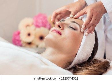 Close-up of the face of a beautiful woman relaxing under the gentle touch of the therapist, during rejuvenating facial massage in a modern beauty center