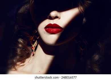 Closeup of the face belong to beautiful young sexy blonde girl with curly hair pure snow white skin and bright makeup red lips, red lipstick, long earrings in dark shadows of palm leaves 
