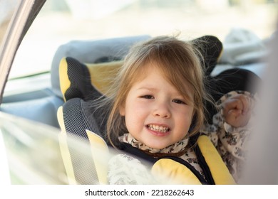 Close-up Face Of Little Child Girl Sitting In A Child Car Seat In The Frame Of The Window