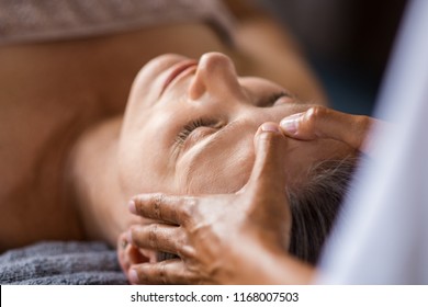 Closeup face of mature woman having facial massage at spa. Senior woman lying at spa while a massage therapist doing anti-aging treatment. Masseur doing head massage at wellness center. - Powered by Shutterstock