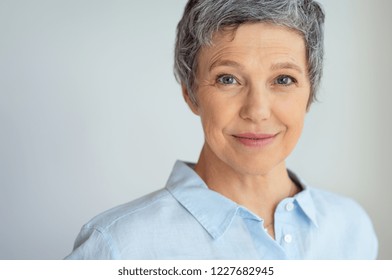 Closeup face of senior business woman standing against grey background with copy space. Portrait of successful woman in blue shirt feeling confident and looking at camera. Happy mature woman face.