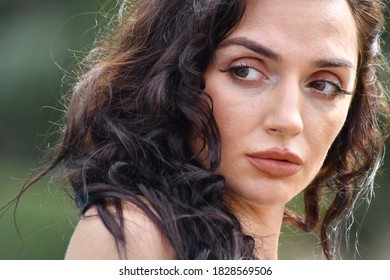Close-up face of a smiling brown-eyed woman looking to the side against the background of an evening public park in summer in sunny weather. - Shutterstock ID 1828569506