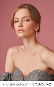 Closeup face studio portait of young elegant blonde caucasian woman with natural makeup and hairstyle wearing jewelry, earrings and posing against pink background. Fashion model