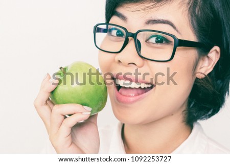 Close-up of face of young Asian woman or dentist wearing eyeglasses eating apple, looking at camera and smiling