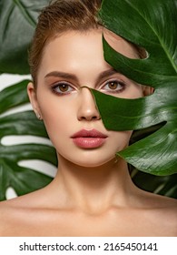 Closeup face of young beautiful woman with a healthy clean skin. Beautiful white girl with big green leaves. Beauty and spa treatment concept. Pretty woman with natural makeup and plant near face - Shutterstock ID 2165450141