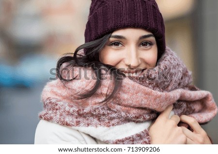 Closeup face of a young happy woman enjoying winter wearing scarf and cap. Smiling girl in a colorful shawl looking at camera. Latin woman with knitted bordeaux hat and woolen scarf.