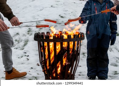 Closeup Of Family At A Campfire Grilling Hot Dog Food. Winter Snow Outdoor Scene.