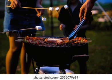 Close-up of Family grills skewers and roasts marshmallows over an open flame during a nighttime barbecue. The scene captures the cozy, festive atmosphere of outdoor cooking while camping - Powered by Shutterstock