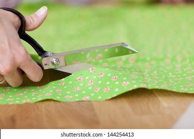 Closeup of fashion designer's hands cutting cloth with scissors in workshop