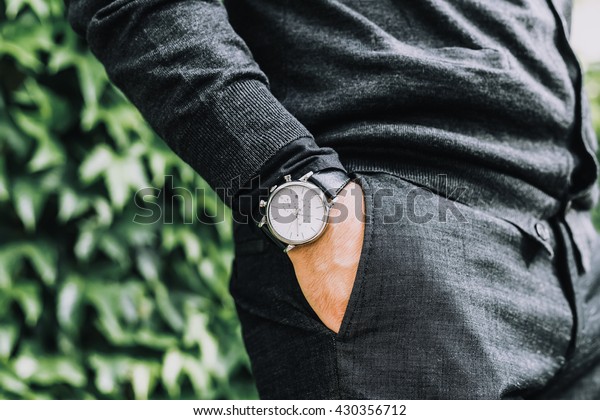 closeup fashion image\
of luxury watch on wrist of man.body detail of a business man.Man\'s\
hand in a grey shirt with cufflinks in a pants pocket closeup.\
Tonal correction 