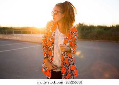 Close-up fashion portrait of young stylish hipster girl posing at sunset.Free happy woman,in trendy summer outfit.Young adult enjoying breathing freely fresh air.Urban background,fashionista,blogger
