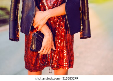 Close-up fashion portrait of young stylish hipster girl posing at sunset,stylish woman's look,leather jacket,party handbag,toned colors,soft vintage colors,red dress,cocktail dress,fashion object 