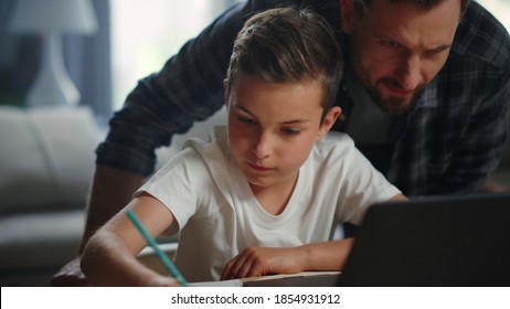 Closeup Father Helping Son Doing Homework In Living Room. Smiling Child And Parent Looking Computer Screen At Home. Positive Man Standing Behind Back Of Boy During Distance Learning Online Indoors.