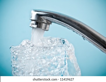 Close-up Of Faucet Pouring Water Into Glass. Blue Tone. Shallow DOF.