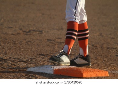 A Close-up Of The Feet Of A Baseball Player As He Stands On First Base In An Image With Room For Copy On The Left Side Of The Frame.