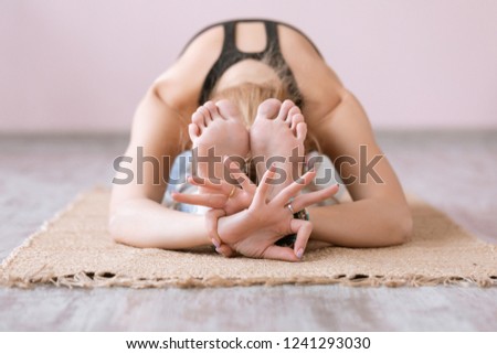 Close-up of feet and hands of attractive sporty young woman practicing yoga indoor on wooden floor on bamboo mat. Beautiful fitness girl doing yoga asana in class. Healthy lifestyle, calmness, relax